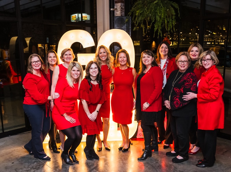 Group of twelve women in red in front of Go Red sign