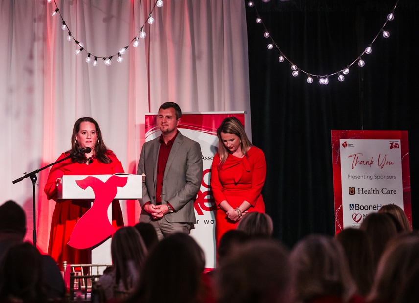 Man and two women in red standing at podium