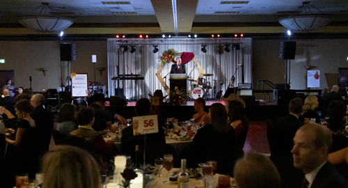 Man on stage speaking to crowded ballroom.